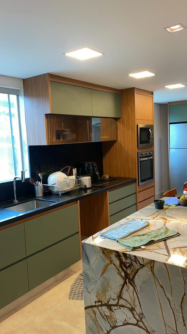 Cozinha planejada verde com madeira e ilha em pedra natural